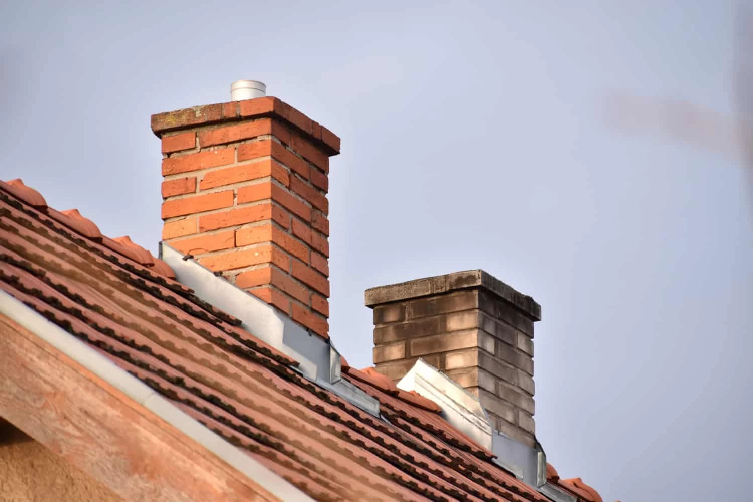 A view of several chimneys rising from a rooftop against a clear blue sky.