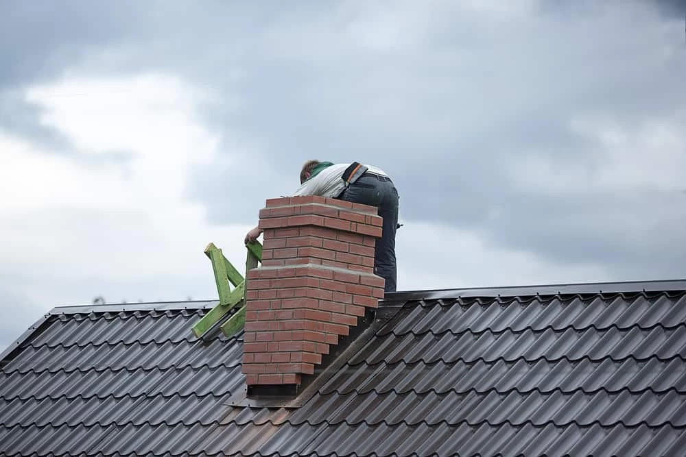 Worker on roof performing brick chimney repair